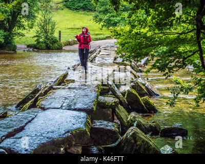Young girl looks skywards wondering when the rain will stop on Tarr Steps in Exmoor, Somerset. Stock Photo