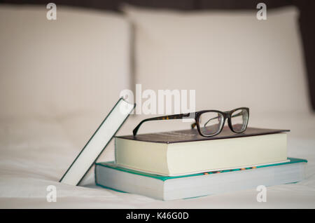 Books on the white bed, glasses on top. Stock Photo