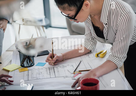 Concentrated asian businesswoman in eyeglasses working with blueprint in office Stock Photo