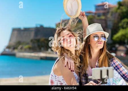 Two smiling young women sitting on a city bench making faces while taking self portraits together Stock Photo