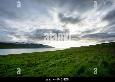 Iceland - Magical cloud formations over lake behind green glowing fields at dawn in summer Stock Photo