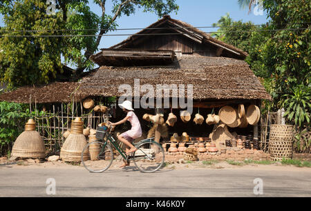 Girl rides past village basket shop in rural Bilugyun, Myanmar Stock Photo