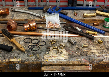 Very well used looking plumbing tools with copper pipe and fittings on an old workshop bench Stock Photo