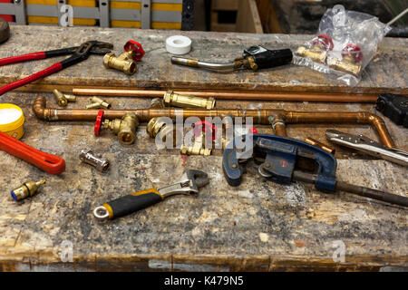 Various plumbing tools and an assortment of fittings and valves on an old workbench Stock Photo