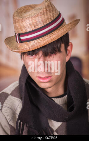 Close up of a sad homeless young man in the streets, wearing a hat and a scarf, in a blurred background Stock Photo