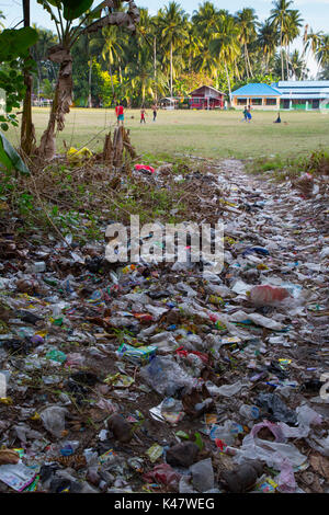Plastic trash and other garbage lying on ground with children playing football behind at Derawan Island, Kalimantan Stock Photo