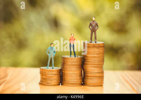 Miniature people, small figures businessmen and woman on top of coins. Money and Financial, Business Growth concept. shallow focus in soft tone. Stock Photo