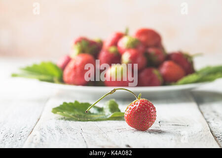 Heap of fresh strawberries in a bowl with leaves and cream on white wooden background. Stock Photo