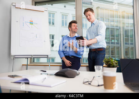 Businessmen Communicating Over Digital Tablet Against Window Stock Photo