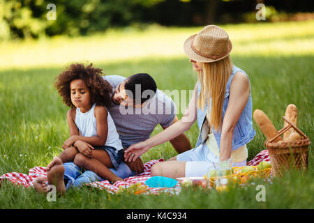 Offended little girl sitting with parents on picnic Stock Photo