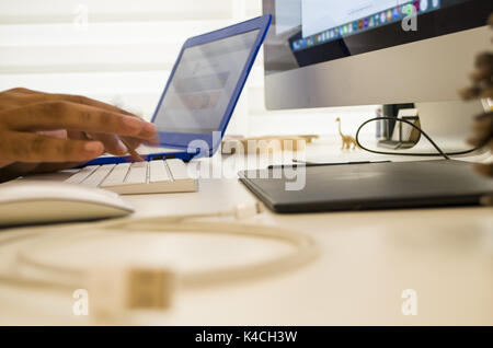 The young man works with the desk and two computers. Keyboard, mouse, charging cord, cone, toy on the table Stock Photo