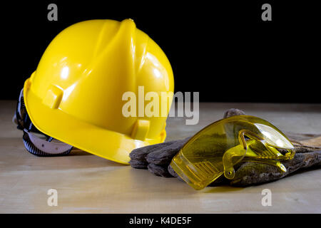 Yellow helmet, safety goggles and work gloves for the worker, black background Stock Photo