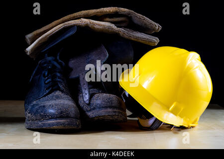 Muddy working boots with helmet and gloves. Accessories for the worker. Black background. Stock Photo