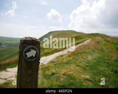 Wooden footpath marker on a pathway, with the peak of Mam Tor in the background. Peak District National Park, Derbyshire Stock Photo