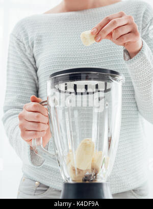 Woman putting a banana in a blender and preparing a delicious healthy smoothie in her kitchen Stock Photo