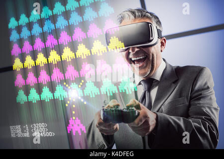 Businessman enjoying virtual reality gaming, he is wearing a VR headset and playing with a videogame controller Stock Photo