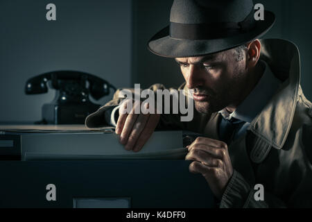 Vintage undercover criminal spy stealing files in a filing cabinet late at night, security and data theft concept Stock Photo