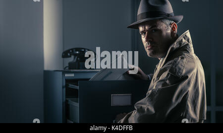 Vintage undercover spy stealing files in a filing cabinet late at night, security, data theft and crime concept Stock Photo