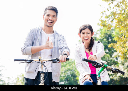 Young Asian couple laughing together while riding bicycles  Stock Photo