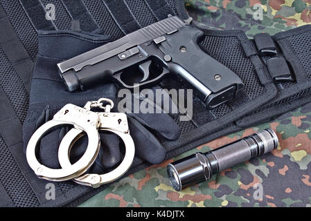 Handgun with handcuffs, gloves and flashlight on black tactical vest and camouflage clothing Stock Photo