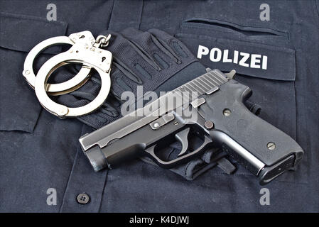 Handgun with handcuffs and gloves on blue uniform shirt with 'Police' in German on it Stock Photo