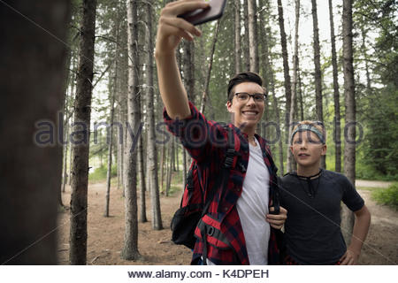 Smiling teenage boy friends with camera phone taking selfie, hiking in woods
