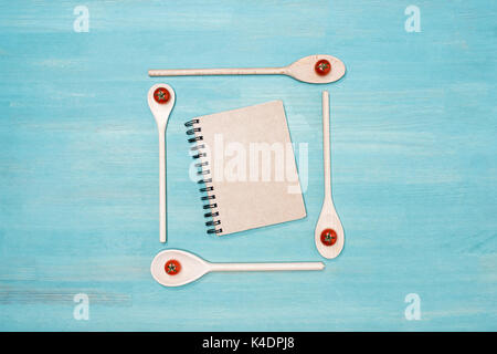 Top view of wooden spoons with cherry tomatoes and closed cookbook with blank cover on wooden table Stock Photo