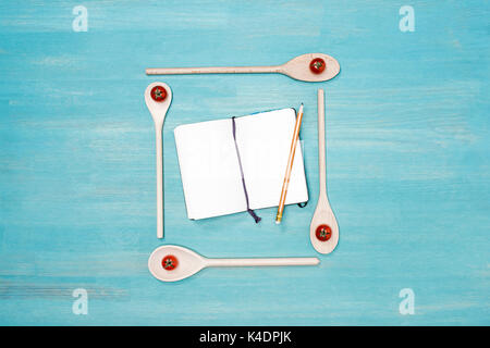 Top view of wooden spoons with cherry tomatoes and blank open cookbook with pencil on table Stock Photo