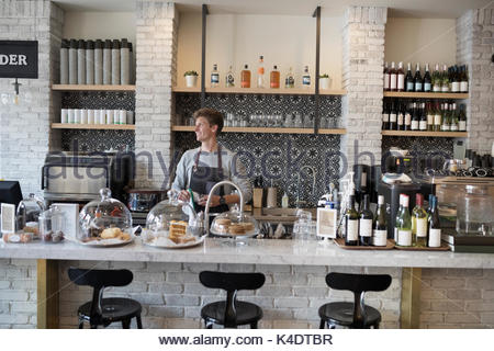 Pensive male cafe owner working behind counter, looking away