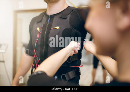 Cropped portrait of woman helping man with putting ems suit on Stock Photo