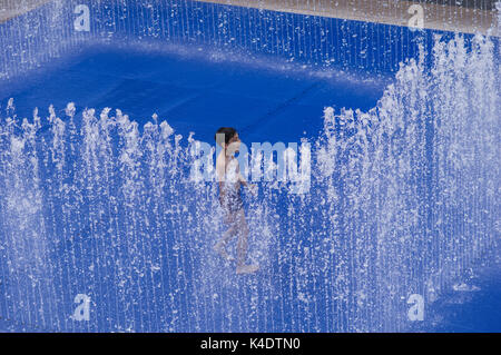 Happy boy playing outside in the Southbank Centre Appearing Rooms water fountain with its blue background Stock Photo