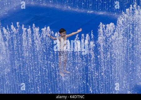 Happy boy playing outside in the Southbank Centre Appearing Rooms water fountain with its blue background Stock Photo