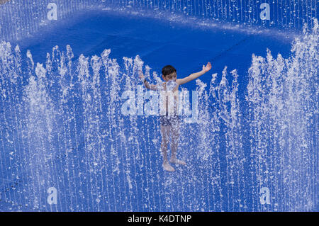 Happy boy playing outside in the Southbank Centre Appearing Rooms water fountain with its blue background Stock Photo