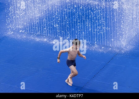 Happy boy playing outside in the Southbank Centre Appearing Rooms water fountain with its blue background Stock Photo