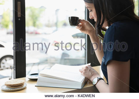 Woman reading book and drinking espresso coffee at cafe window