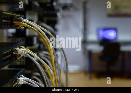 RJ45 cables plugged into switches in rack with work space on background Stock Photo