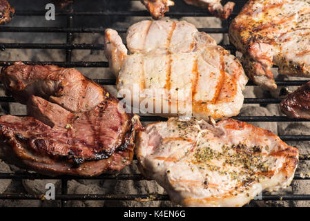 Seasoned pork chops and lamb steak cooking on the charcoal bbq grill. Stock Photo