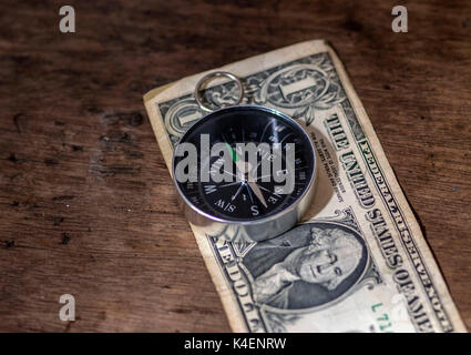 Navigation compass on top of a one dollar bill, and a wooden background, money and direction concept Stock Photo