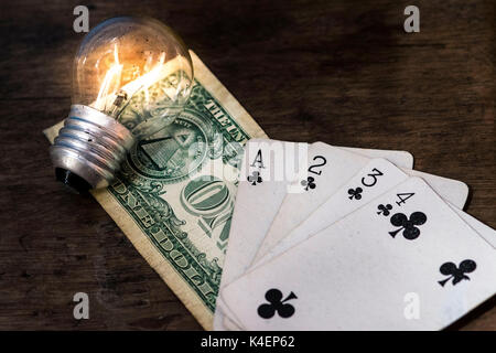 Lit light bulb, US money one dollar bill and white playing cards, face up, on top of a wooden surface, money, gambling and winning concept idea Stock Photo