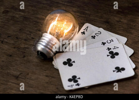 Lit light bulb and white playing cards, face up, on top of a wooden surface, gambling and winning concept idea Stock Photo