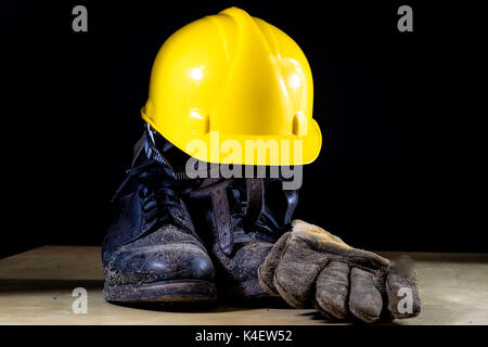 Muddy working boots with helmet and gloves. Accessories for the worker. Black background. Stock Photo