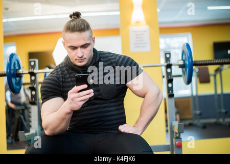 Young handsome man using phone while having exercise break in gym Stock Photo
