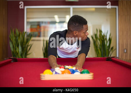 Closeup portrait, young man hanging out, playing billiards at red pool table, isolated indoors background Stock Photo