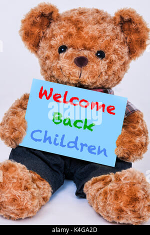 Cute teddy bear holding a blue sign hte says Welcome back Children isolated on a white background Stock Photo