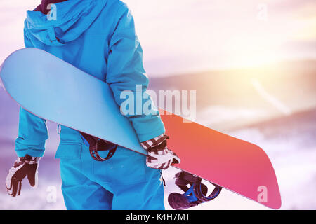 Woman holding snowboard in hands. Closeup view. Snowboarder or snowboarding concept at sunrise or sunset time Stock Photo