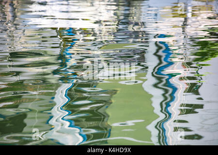 Water reflections, sailing boat masts shapes mirrored in a sea or ocean waters. Image blurred by water. Background photo. Stock Photo