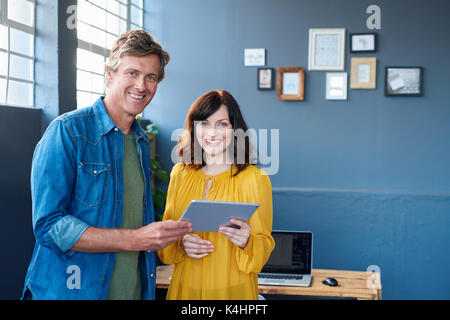 Portrait of two confident young office colleagues working together while standing in a modern office using a digital tablet Stock Photo