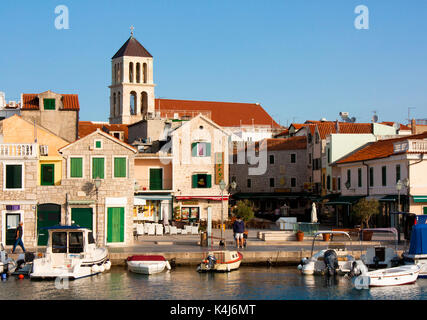 Vodice, Croatia - August 22, 2017: Sunny morning in small Mediterranean town square with stone houses and old church tower. with moored boats on the d Stock Photo