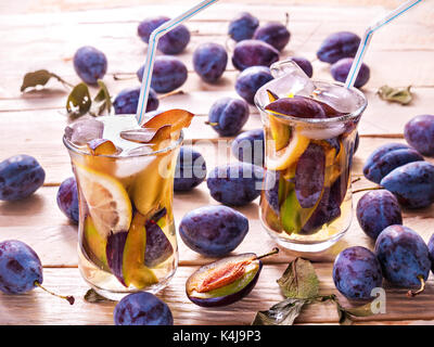 Refreshing drink from fresh juicy sweet plums with lemon in glass mugs with ice cubes on a wooden background with plums and green leaves Stock Photo