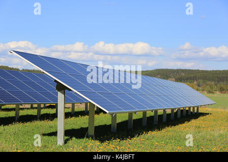 Solar panels on a field of grass and flowers on a sunny day of spring with blue sky and clouds. Stock Photo